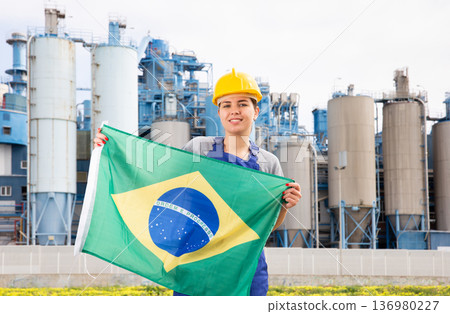 Young female engineer in helmet waving state flag of Brazil while standing in front of big tanks at chemical plant Young female engineer in helmet waving state flag of Brazil while standing in front of big tanks at chemical plant 136980227
