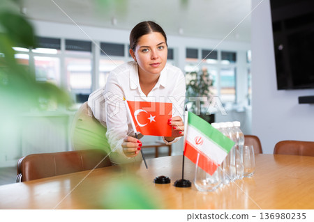 Positive young woman putting little flag of Turkey on table next to the flag of Iran Positive young woman putting little flag of Turkey on table next to the flag of Iran 136980235