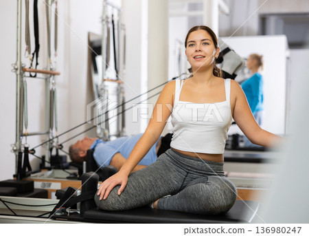 Positive young female performing mermaid exercise on reformer Pilates machine in studio 136980247