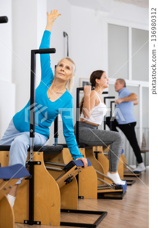 Concentrated mature female practicing Pilates system on Wanda chair machine in studio to improve mobility of upper back Concentrated mature female practicing Pilates system on Wanda chair machine in studio to improve mobility of upper back 136980312