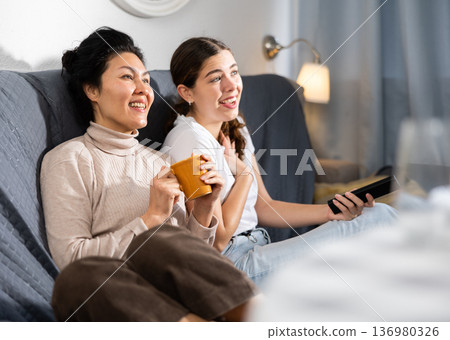 Positive women sitting on couch and watching TV together 136980326