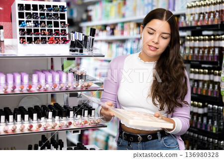 Positive woman choosing face powder on color palette in cosmetics store 136980328