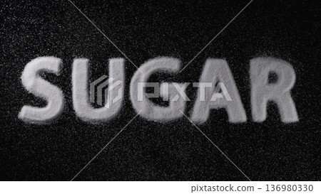 Sugar spelled out with white granules on a dark surface showcasing the texture and contrast of the material 136980330