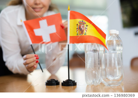 Little flag of Spain on table and flag of Switzerland put next to it by young woman 136980369