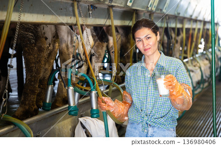 Asian woman dairy farm worker standing with glass of milk Asian woman dairy farm worker standing with glass of milk 136980406