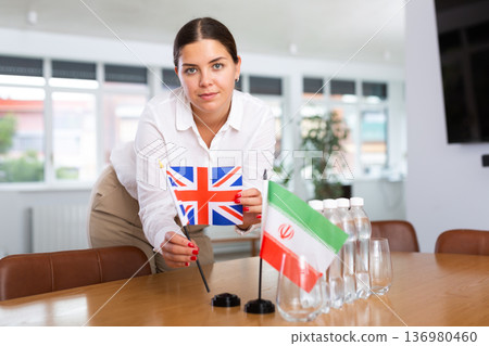 Positive young woman putting little flag of Great Britain on table next to the flag of Iran Positive young woman putting little flag of Great Britain on table next to the flag of Iran 136980460