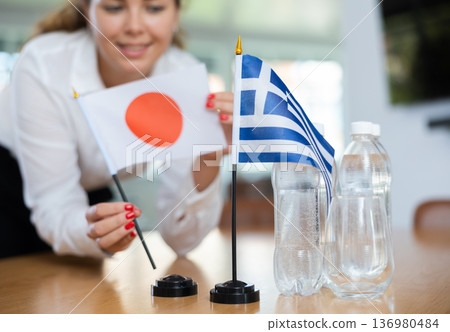 Unrecognizable girl sets midget flags of Greece and Japan before international negotiations Unrecognizable girl sets midget flags of Greece and Japan before international negotiations 136980484