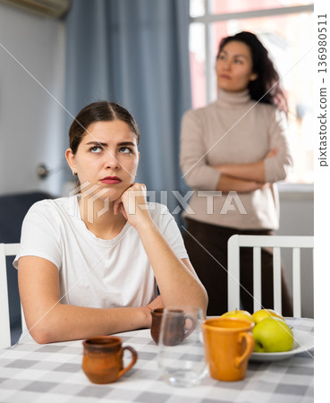 Woman sitting at table at home while having quarrel with her friend 136980511