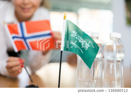 Woman secretary prepares an office for negotiations - she places flags of Saudi Arabia and Norway table 136980512