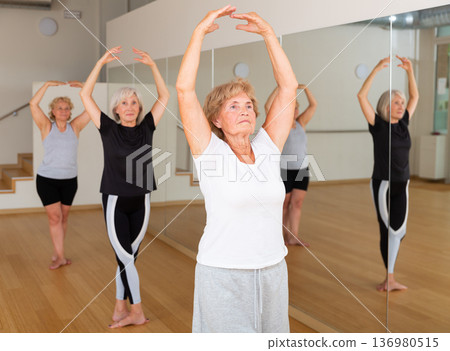 Mature women performing ballet dance in exercise room Mature women performing ballet dance in exercise room 136980515