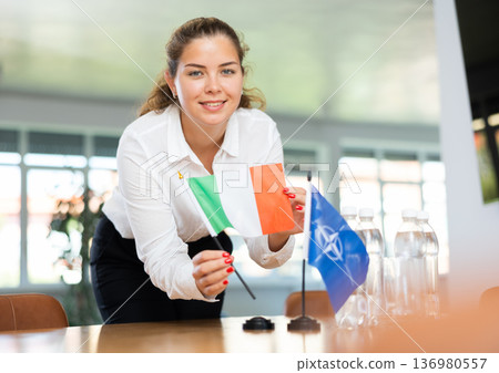 Young female secretary preparing room for international negotiations between nato and italy Young female secretary preparing room for international negotiations between nato and italy 136980557