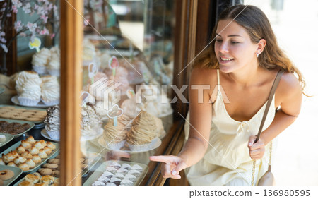Young tourist girl near window of street cafe food court chooses stuffed puff and cookie Young tourist girl near window of street cafe food court chooses stuffed puff and cookie 136980595