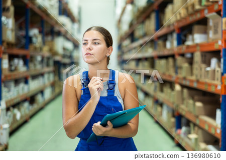 Attentive female manager keeps records of construction materials in warehouse, writing down data on paper Attentive female manager keeps records of construction materials in warehouse, writing down data on paper 136980610