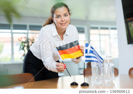 Young female secretary preparing room for international negotiations between greece and germany Young female secretary preparing room for international negotiations between greece and germany 136980612