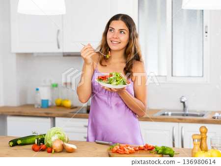 Smiling young woman eating salad at home Smiling young woman eating salad at home 136980614