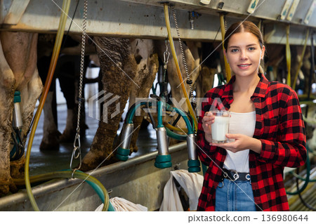 Female milker posing with glass of milk on dairy farm Female milker posing with glass of milk on dairy farm 136980644