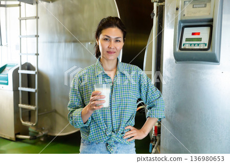 Asian woman with glass of milk standing near tanks 136980653