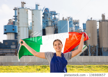 Happy young woman worker with flag of Italy against background of factory Happy young woman worker with flag of Italy against background of factory 136980657