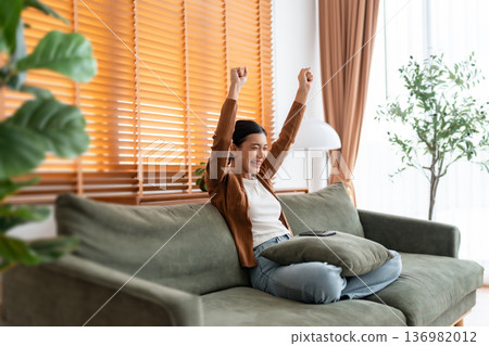 Happy young asian woman relax on comfortable couch at home texting messaging on smartphone 136982012