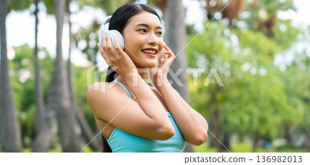 Asian sports woman listening to music on headphones outdoors 136982013