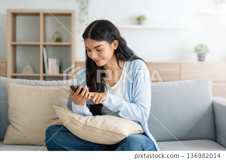 Smiling pretty young Asian woman sitting on cozy couch 136982014
