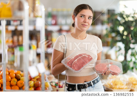 Young woman in store took raw beef steak and hamburger cutlet, choose meat Young woman in store took raw beef steak and hamburger cutlet, choose meat 136982555
