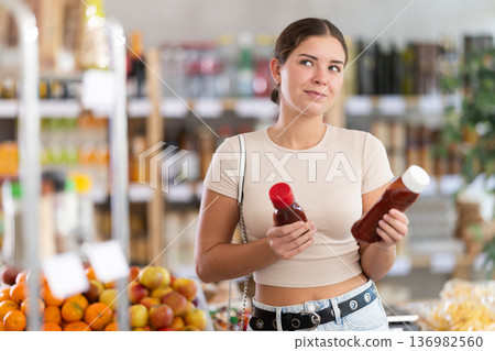Young woman choosing ketchup in grocery store Young woman choosing ketchup in grocery store 136982560
