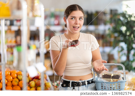 European girl with basket of groceries in hands stands in store and dictates audio message 136982574