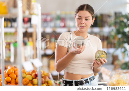 Young woman is holding two tin cans of preserves in hands, choosing pate for sandwiches. Young woman is holding two tin cans of preserves in hands, choosing pate for sandwiches. 136982611