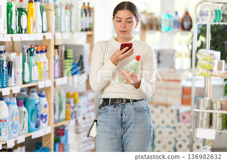 Before making purchase, young woman buyer scans QR code on packaging of dishwashing detergent 136982632