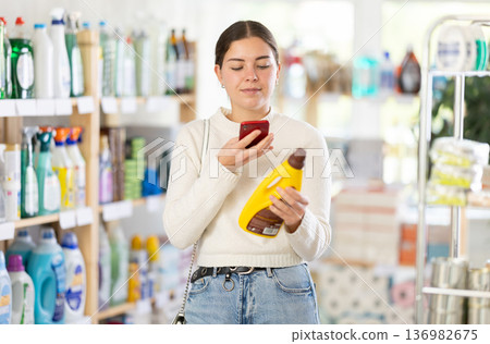 Before making purchase, girl buyer scan QR code on packaging of polishing agent for wooden furniture Before making purchase, girl buyer scan QR code on packaging of polishing agent for wooden furniture 136982675