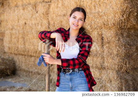 Hired cow farm worker posing in barn against background of hay bales 136982709