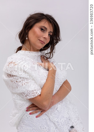 Confident woman in white dress standing with crossed arms, assertive expression and poised stance, editorial corporate aesthetic with subtle jewelry and strong presence 136983720