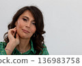 Contemplative woman refining her ear adornment elegantly, Professional studio photography capturing woman with soft hair and confident demeanor focusing on her accessory 136983758
