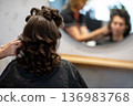 Stylist adding finishing touches to curled hair, last checks in mirror, subtle smoothing and shaping, anticipation of final look, organized station in background 136983768