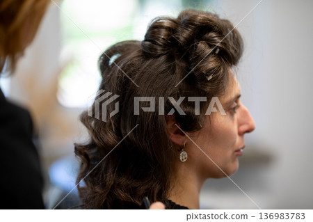 Woman in profile listening intently at concert, soft stage lighting, intricate updo, small earring visible, blurred crowd behind, grainy film texture, quiet contemplative mood 136983783