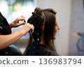 Calm atmosphere during hair styling process, Closeup of stylist working on damp hair in salon, Candid scene showing stylist carefully braiding damp hair with warm lighting 136983794