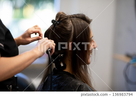 Calm atmosphere during hair styling process, Closeup of stylist working on damp hair in salon, Candid scene showing stylist carefully braiding damp hair with warm lighting 136983794