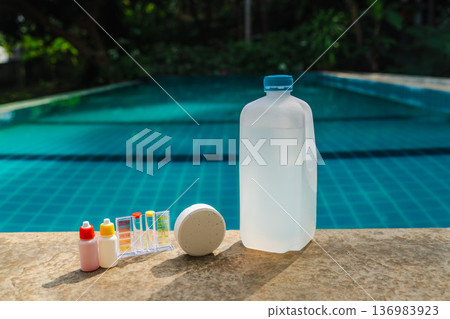 Pool water testing kit, chlorine tablet and chemical container on swimming pool edge with turquoise water background, pool maintenance and sanitation concept  136983923