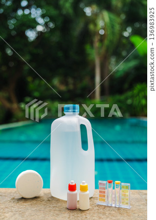 Pool maintenance kit with chlorine tablet, chemical bottles and water testing kit on pool edge, clean swimming pool background with copy space Pool maintenance kit with chlorine tablet, chemical bottles and water testing kit on pool edge, clean swimming pool background with copy space 136983925