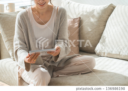 A stylish Asian woman sitting on the sofa in the living room and reading a magazine 136986198