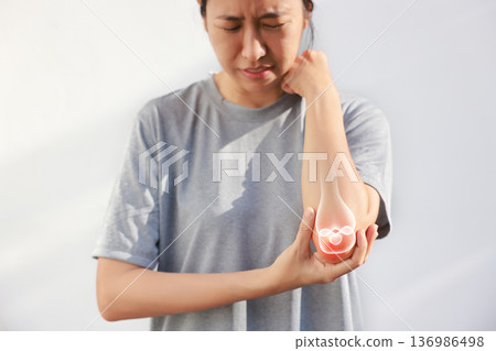 Asian woman suffering from elbow joint pain with red x-ray bone graphic overlay, female touching arm feeling ache from inflammation, arthritis, tendonitis or injury in garden, healthcare concept. 136986498