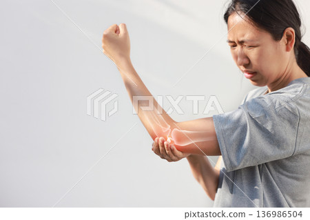 Asian woman suffering from elbow joint pain with red x-ray bone graphic overlay, female touching arm feeling ache from inflammation, arthritis, tendonitis or injury in garden, healthcare concept. Asian woman suffering from elbow joint pain with red x-ray bone graphic overlay, female touching arm feeling ache from inflammation, arthritis, tendonitis or injury in garden, healthcare concept. 136986504