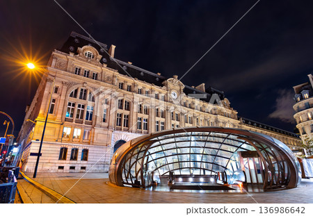 Night view of a modern glass dome metro entrance in front of the illuminated historic Gare Saint Lazare train station building in Paris, France. 136986642