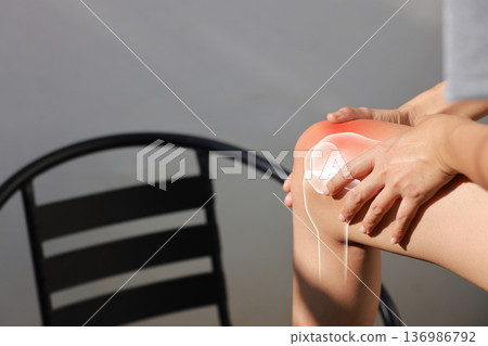 Asian woman sitting on stairs suffering from knee pain with red x-ray bone graphic overlay, female touching leg feeling ache from osteoarthritis, meniscus injury or joint inflammation concept. 136986792