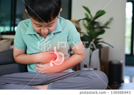 Little boy suffering from stomach ache with x-ray gastric graphic overlay, child holding belly feeling painful from indigestion, gastritis, food poisoning or abdominal pain at home. 136986943