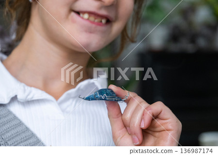 Happy girl holding blue orthodontic plate, removable device for correcting bite and straightening teeth. Happy girl holding blue orthodontic plate, removable device for correcting bite and straightening teeth. 136987174