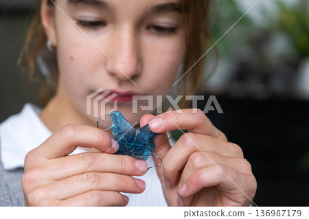 Happy girl holding blue orthodontic expander plate, pediatric device for interceptive bite correction. 136987179