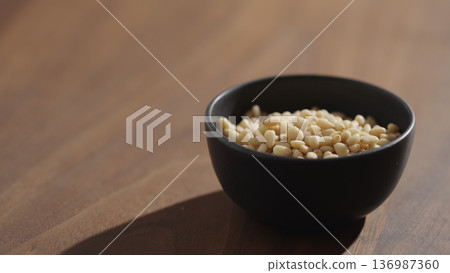 Pine nuts in a black bowl on wood table closeup Pine nuts in a black bowl on wood table closeup 136987360