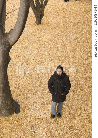 一位身著冬裝的女子站在鋪滿木屑的公園裡。 一位身著冬裝的女子站在鋪滿木屑的公園裡。 136987944